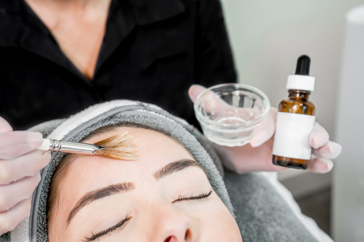 Close up of beautician (cosmetologist) applying chemical peel treatment on patient in a beauty spa, for skin rejuvenation, complexion and acne beauty treatments.