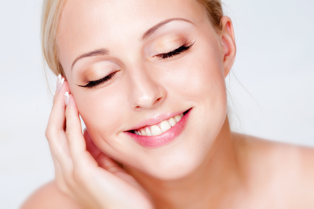Fair-skinned blonde woman touches her soft skin following a laser resurfacing treatment with little downtime.