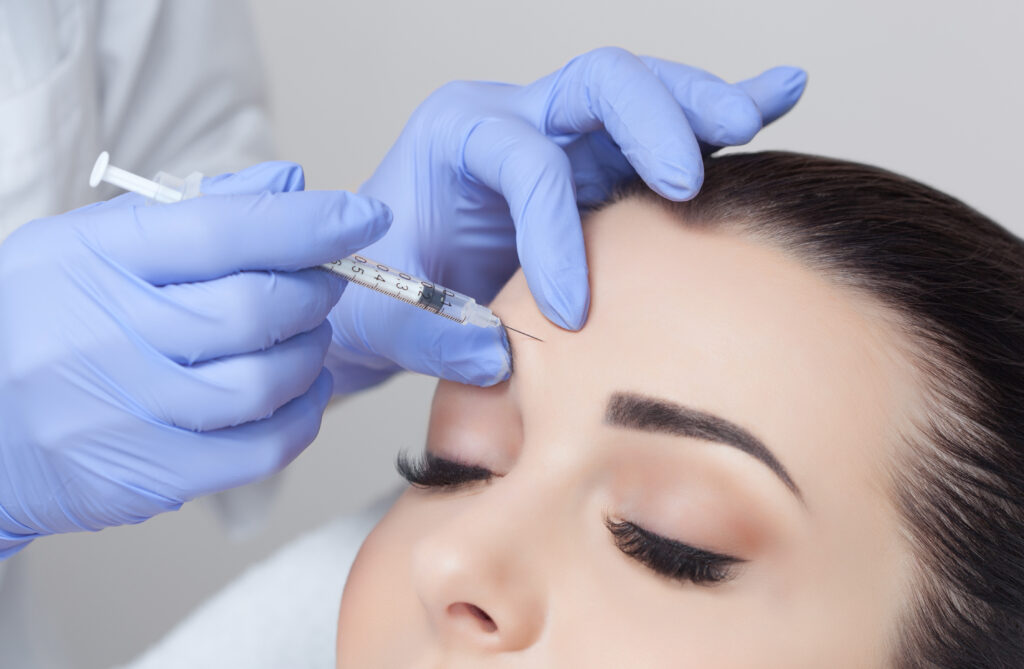 Dark-haired, fair-skinned woman receives a Botox injection on her forehead to relax brow muscles that cause lines