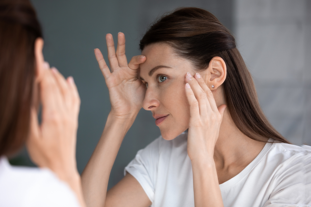 Close-up of woman looking in mirror after beauty treatment, admiring smooth skin following laser resurfacing, glycolic acid peel, and anti-aging skincare.
