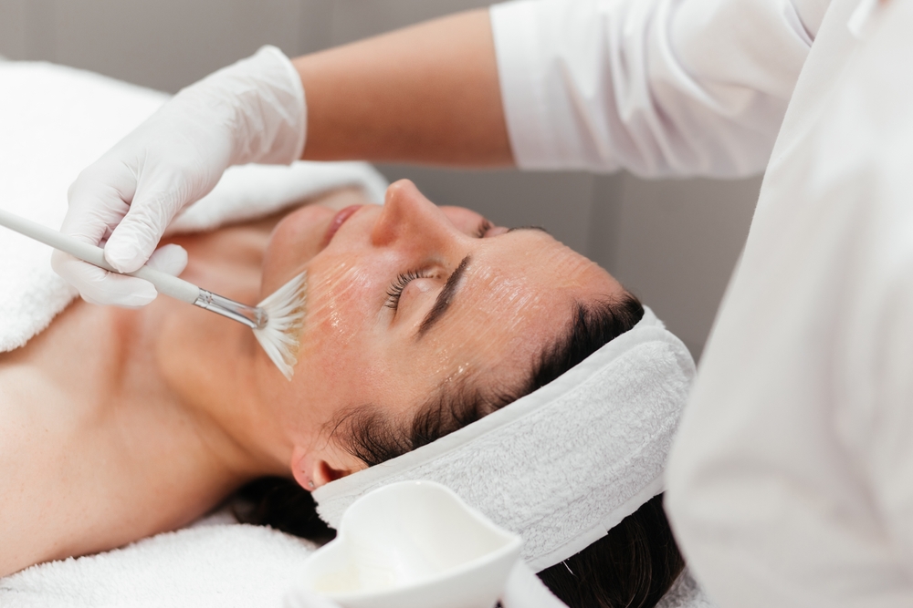 Woman receiving facial chemical peel with retinol mask at beauty salon, concept of anti-aging skincare, rejuvenation, and wellness treatment.