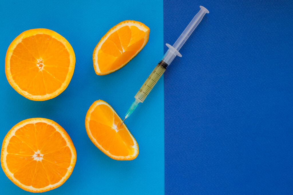 Representation of vitamin shots with a syringe beside oranges