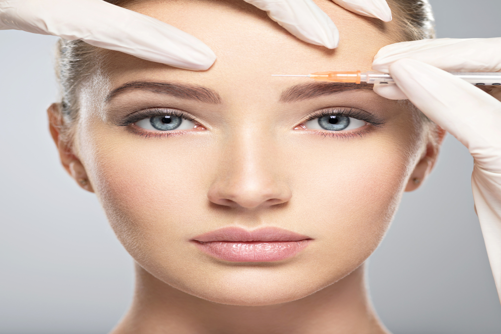 Young blonde woman receives Botox injection to minimize frown lines on forehead