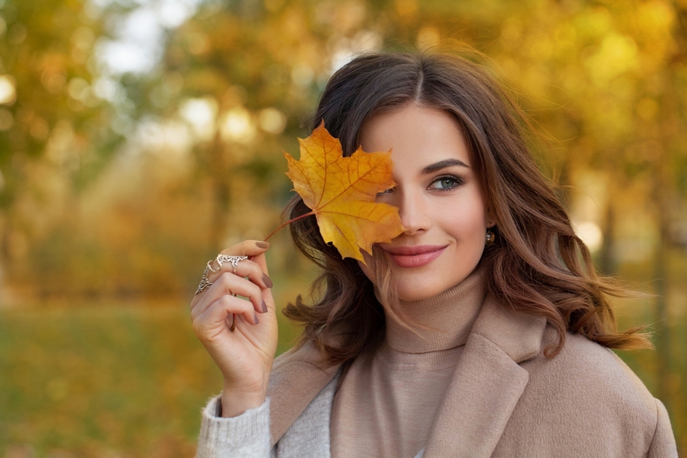 Pretty woman holds a leaf in front of her face.